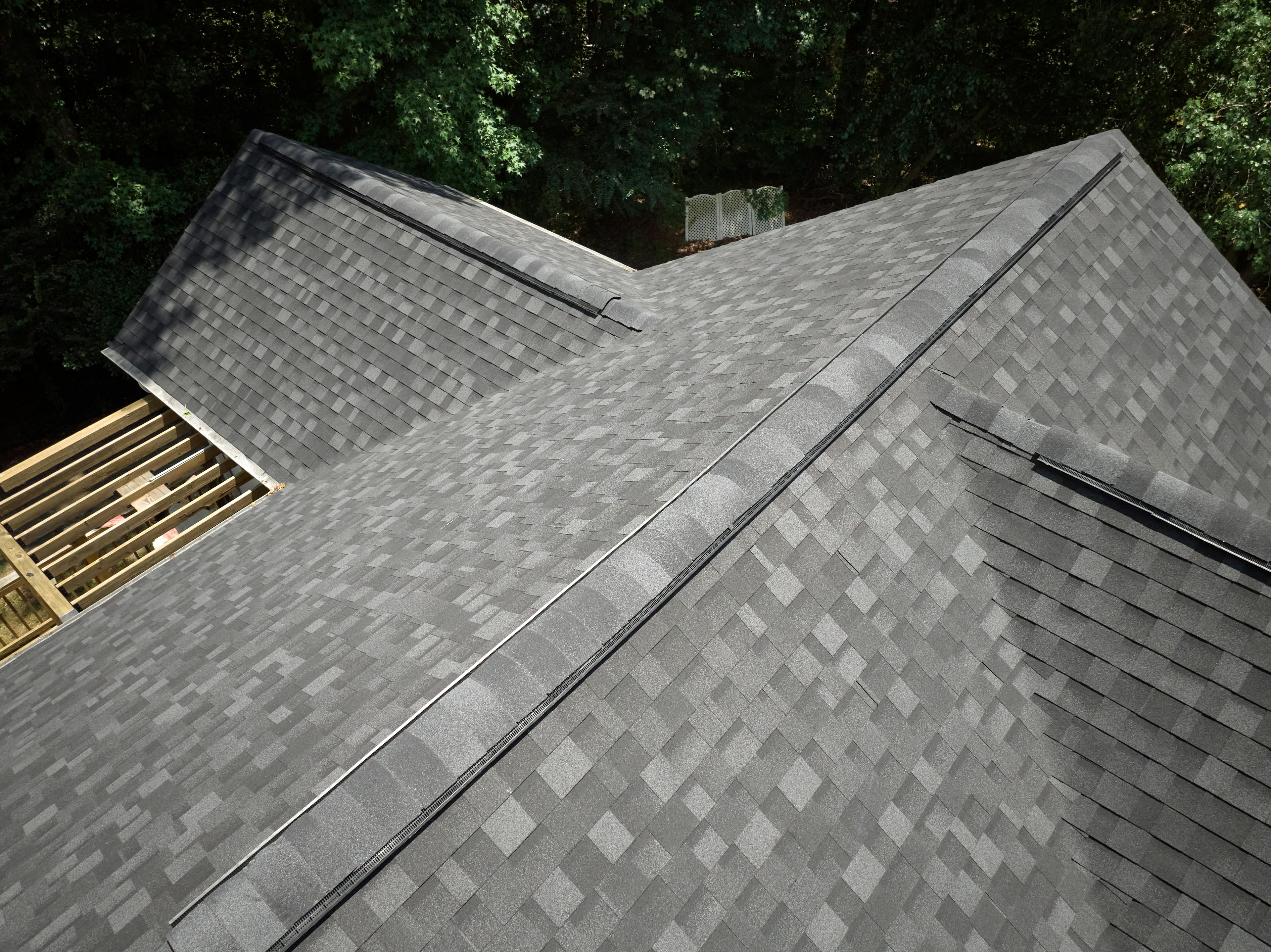 Image from atop a residential roof with granite black aphalt shingles. Green grass and trees in background.