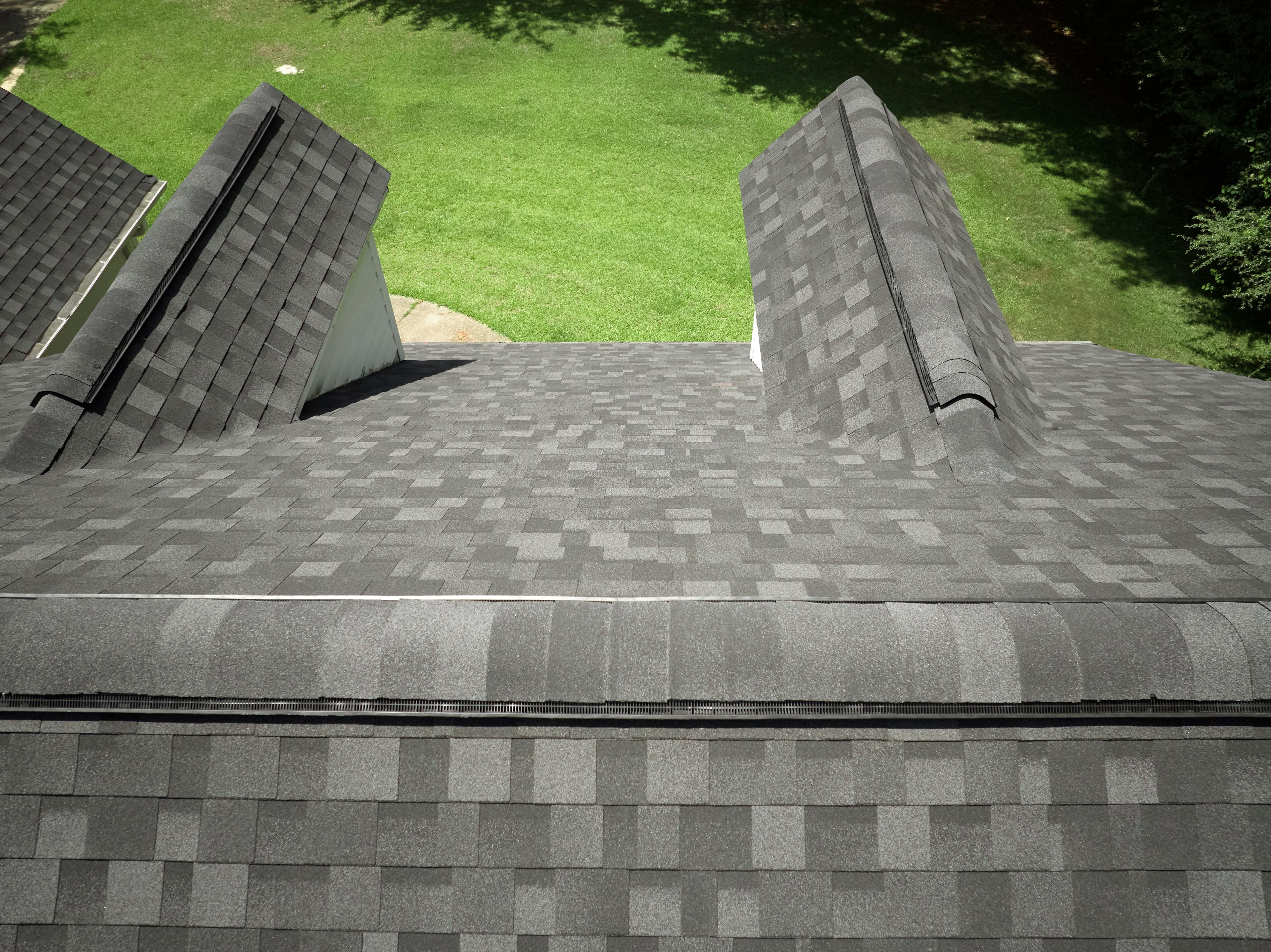 Image from top of a residential roof with granite black aphalt shingles. Green grass yard in background.