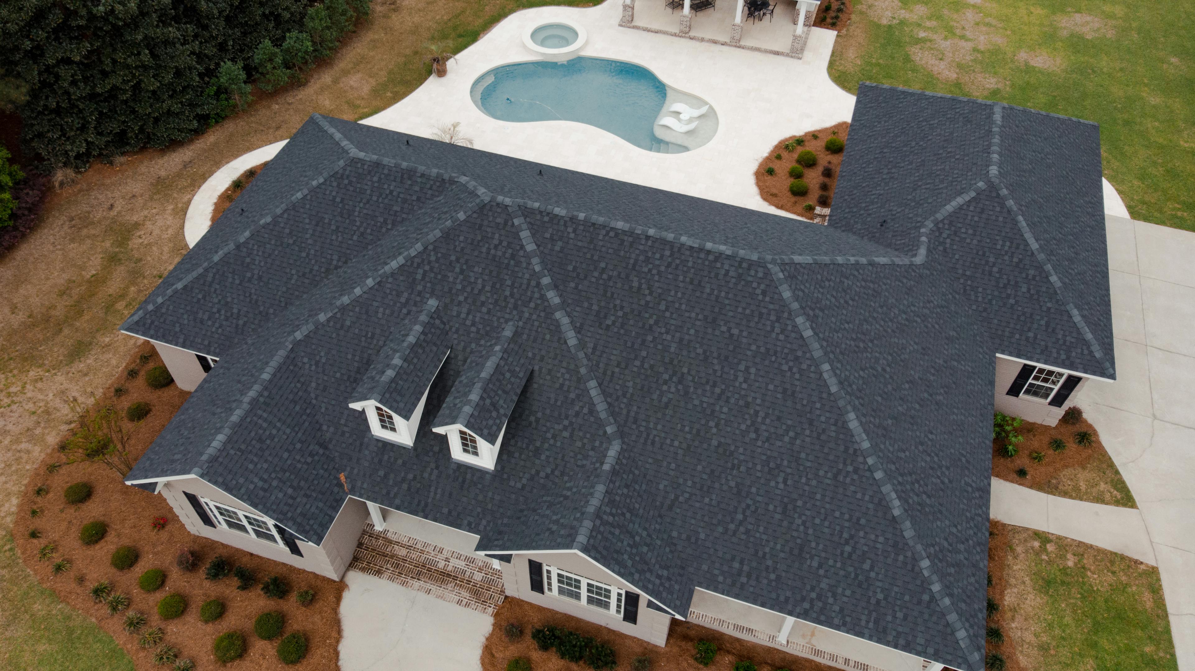 Aerial drone image of residential roofing project. Black asphalt shingles swimming pool and fresh landscaping surrounding home.